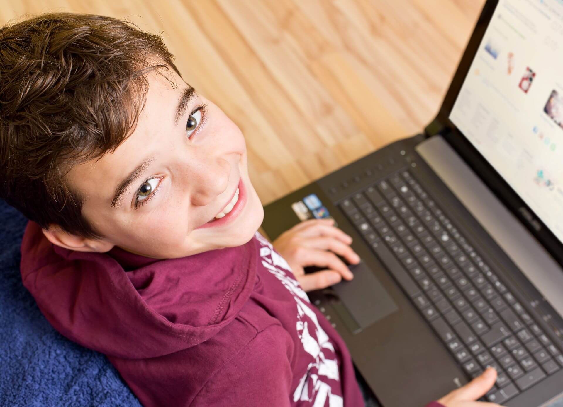 Young smiling boy working at desk with laptop open